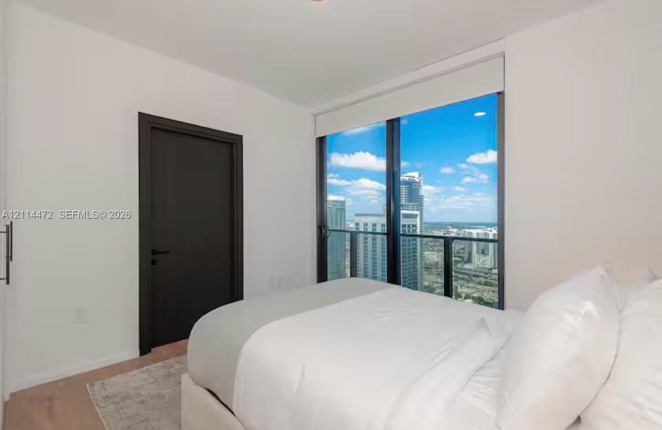 Floor-to-ceiling windows with expansive urban cityscape scenery, dark-finish interior door, recessed lighting, and light-tone wood-finish flooring