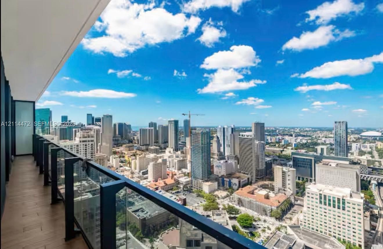 Covered balcony featuring wood-finish flooring and a glass panel railing with metal supports, overlooking an expansive cityscape