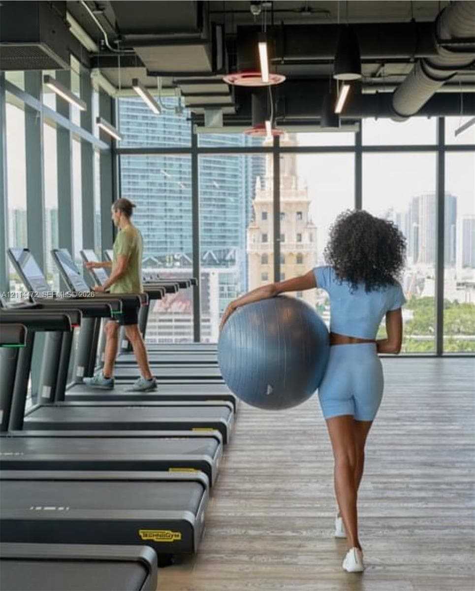 Fitness center featuring floor-to-ceiling windows, wood-finish flooring, exposed industrial-style ceiling, and linear LED lighting
