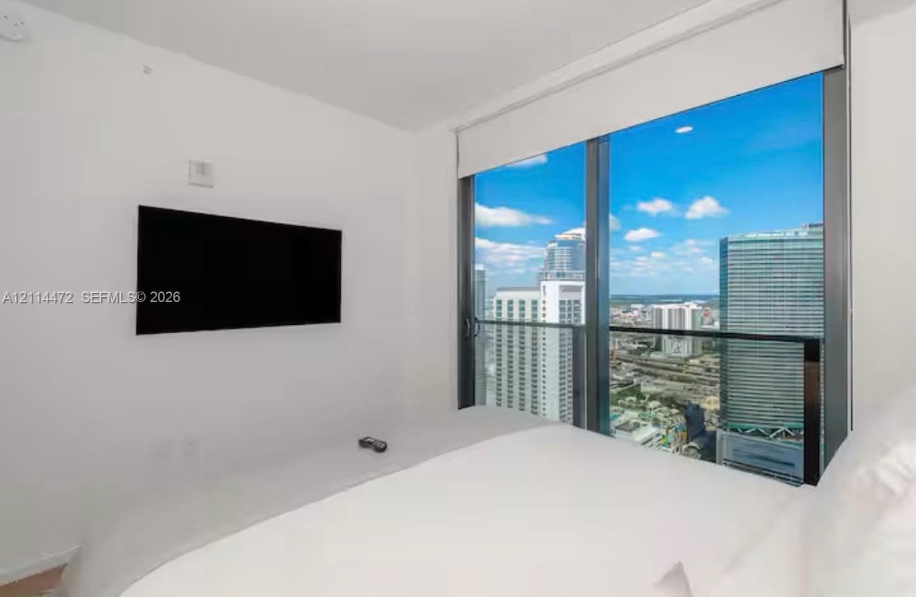 Floor-to-ceiling windows, attached glass-railed balcony, and urban cityscape backdrop