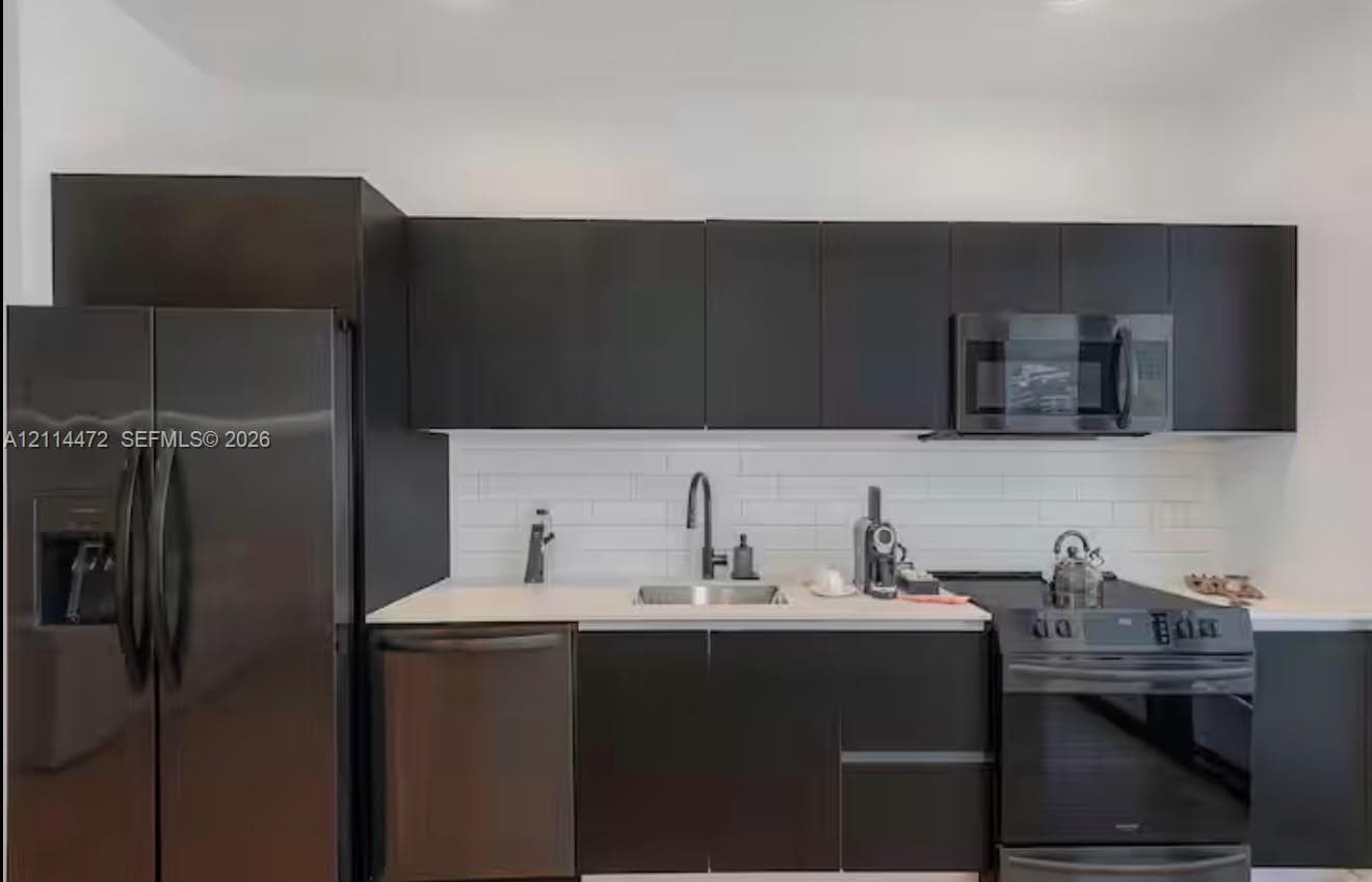 Modern kitchen featuring flat-panel cabinetry, a white subway tile backsplash, light-toned countertops, a stainless steel undermount sink, and matte black hardware