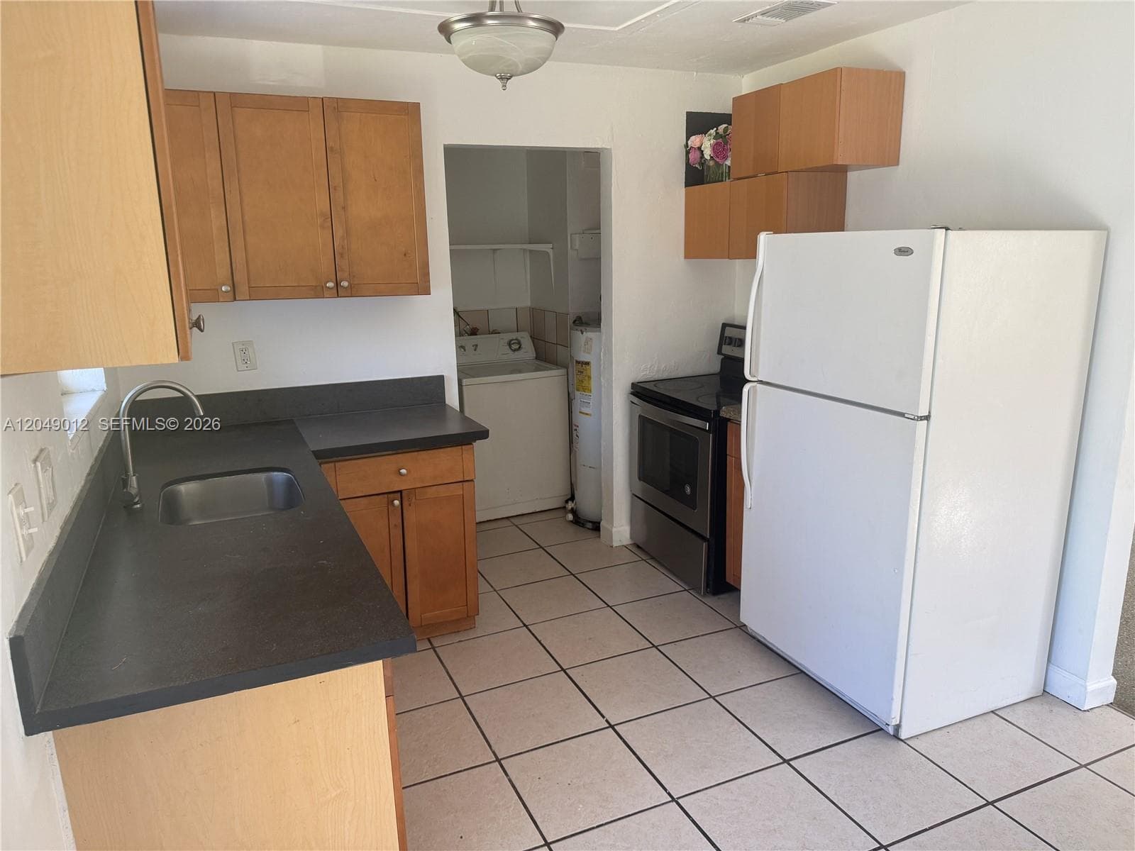 Kitchen featuring flat-panel wood cabinetry, dark solid-surface countertops, square ceramic tile flooring, and a stainless steel sink with a gooseneck faucet