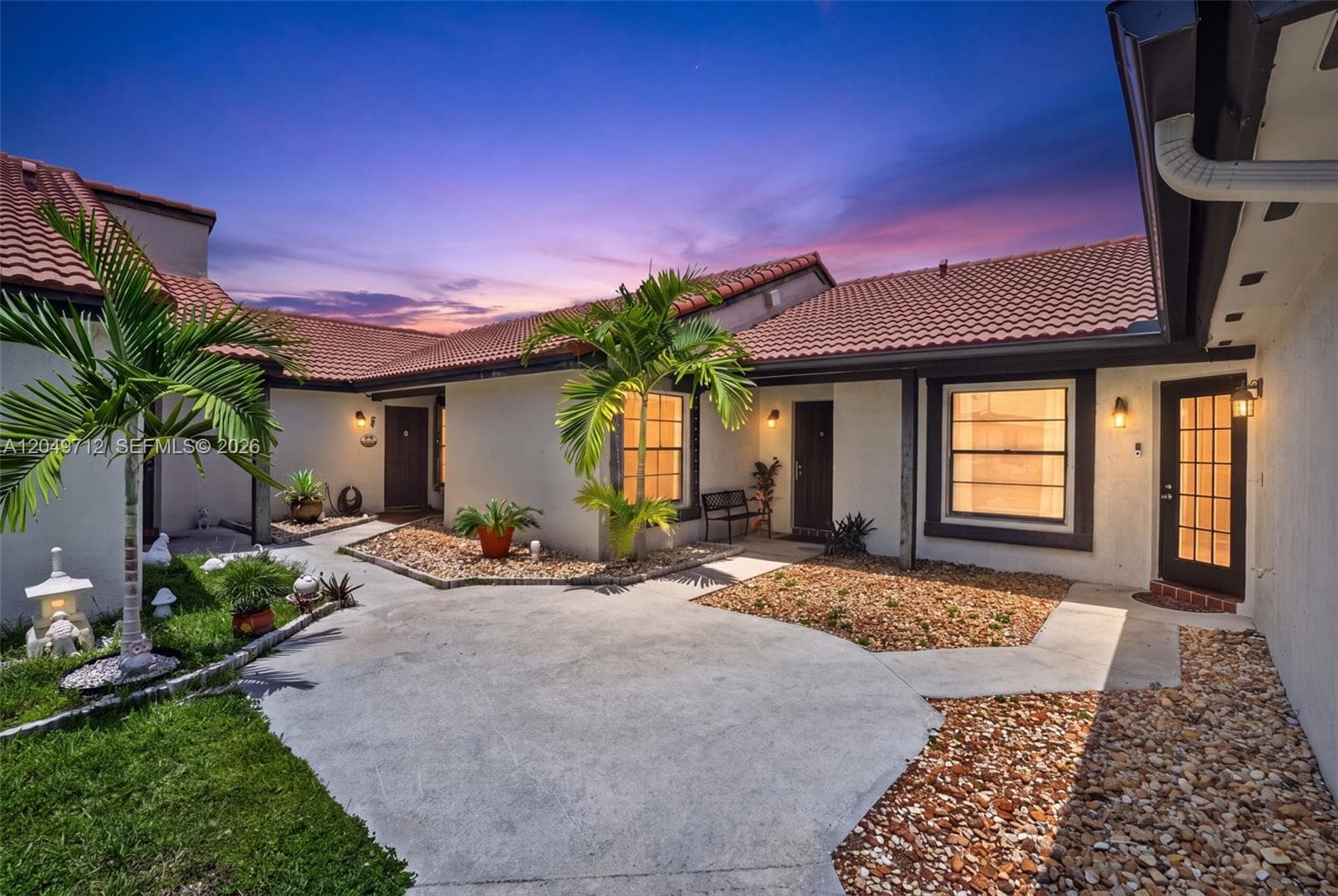 Courtyard entrance featuring a concrete patio, tile roofing, stone ground cover, and exterior wall-mounted lighting