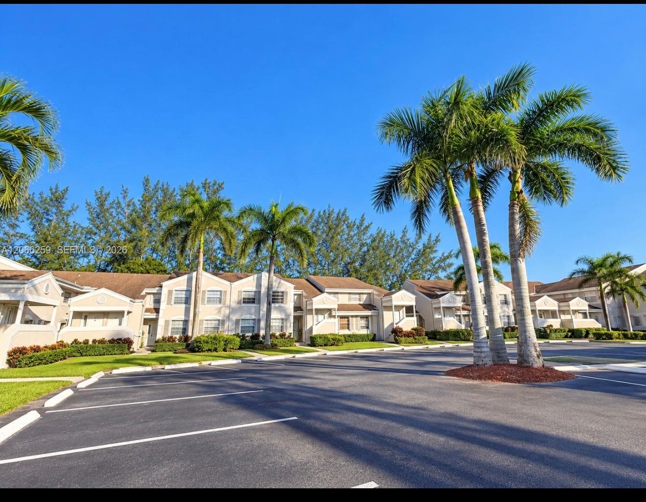 Multi-unit residential complex featuring beige stucco facades, pitched roofing, and paved parking with mature palm landscaping