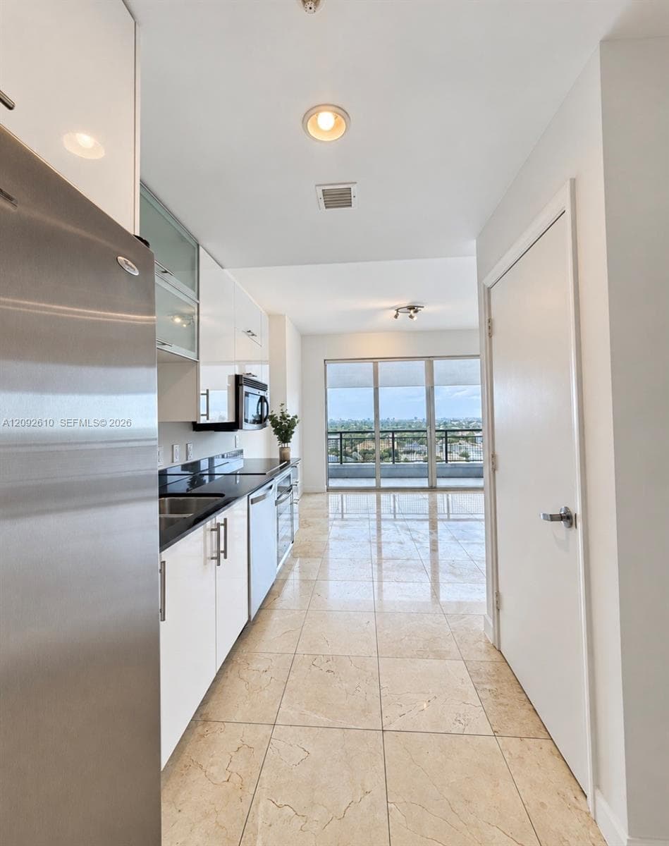Kitchen featuring gloss-finish white cabinetry, dark countertops, stainless steel appliances, and tile flooring, extending to a balcony with exterior railing