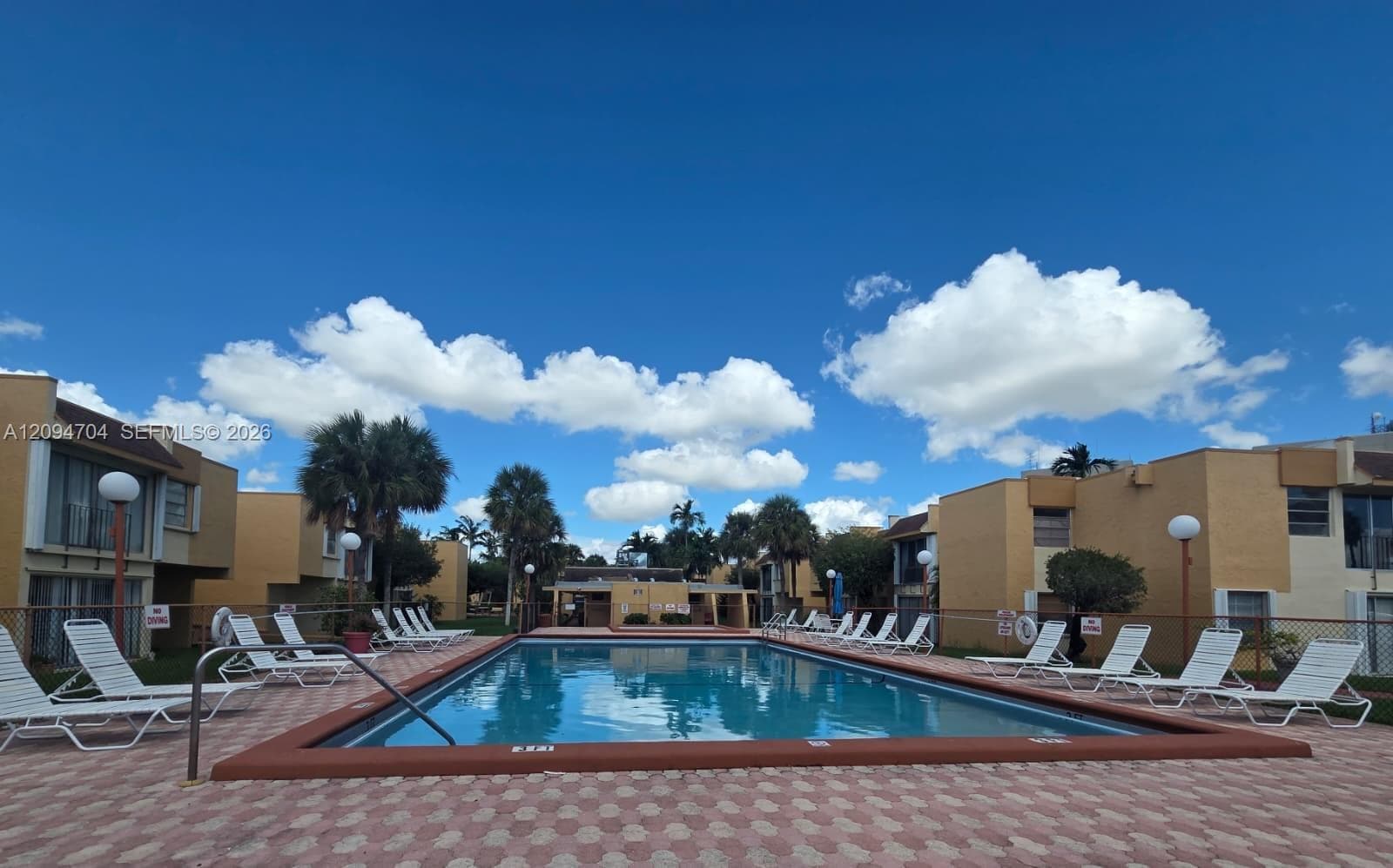 In-ground swimming pool featuring a concrete coping border, paver deck, and surrounding metal fencing