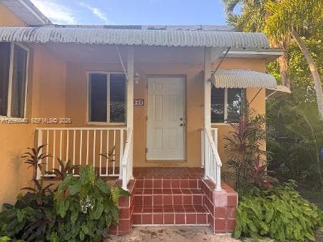 Covered front entry featuring a tiled stoop, white metal railings, and scalloped metal awnings