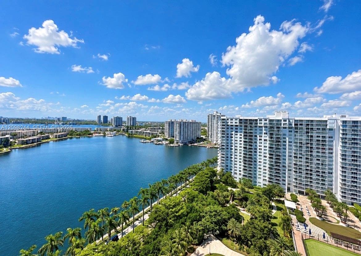 High-rise balcony perspective featuring expansive water frontage, mature palm trees, landscaped grounds, and a paved walkway