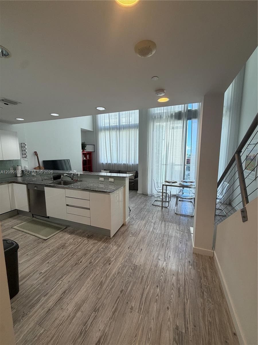 Open-concept kitchen featuring flat-panel cabinetry, stone countertops, stainless steel appliances, wood-finish flooring, and floor-to-ceiling windows