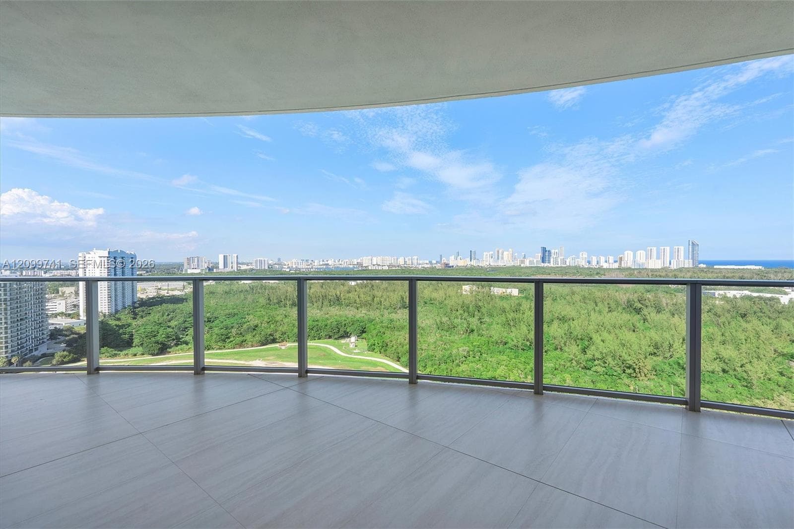 Expansive covered balcony featuring large-format tile flooring and a glass panel railing