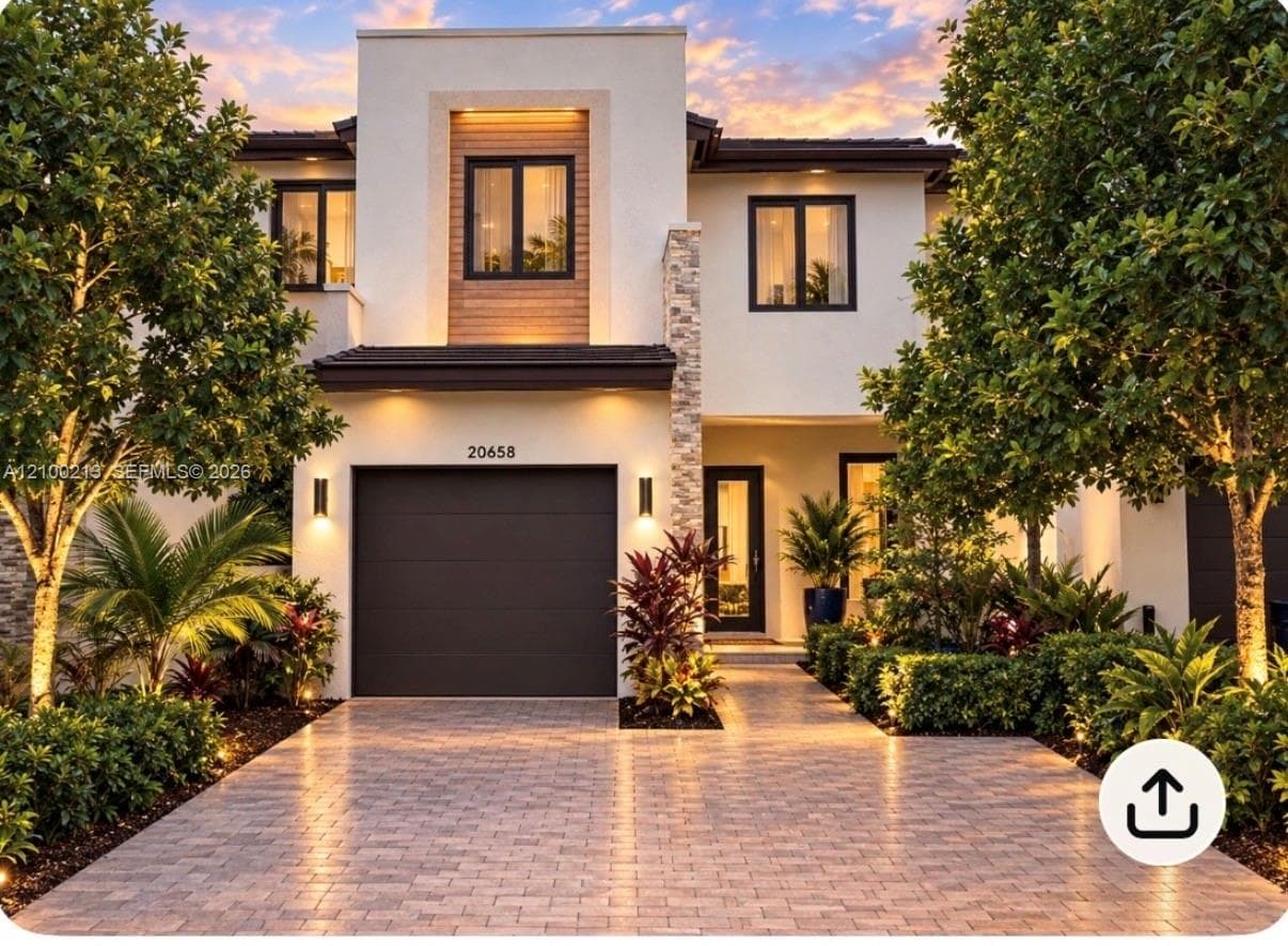 Modern two-story exterior featuring smooth stucco siding, stone veneer accents, wood-finish paneling, a paver driveway, and a solid-panel garage door