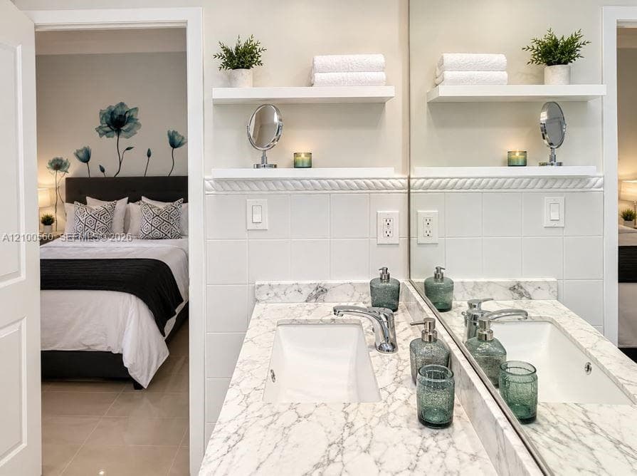 Bathroom featuring a stone-look countertop with an integrated rectangular sink, wall-mounted white floating shelving, and white tile wall accents with decorative molding