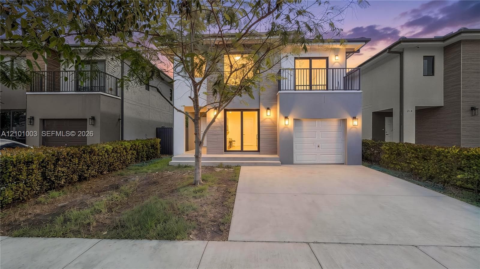 Two-story contemporary exterior featuring a concrete driveway, an attached garage, a second-story balcony with metal railings, and dual-level glass entry doors