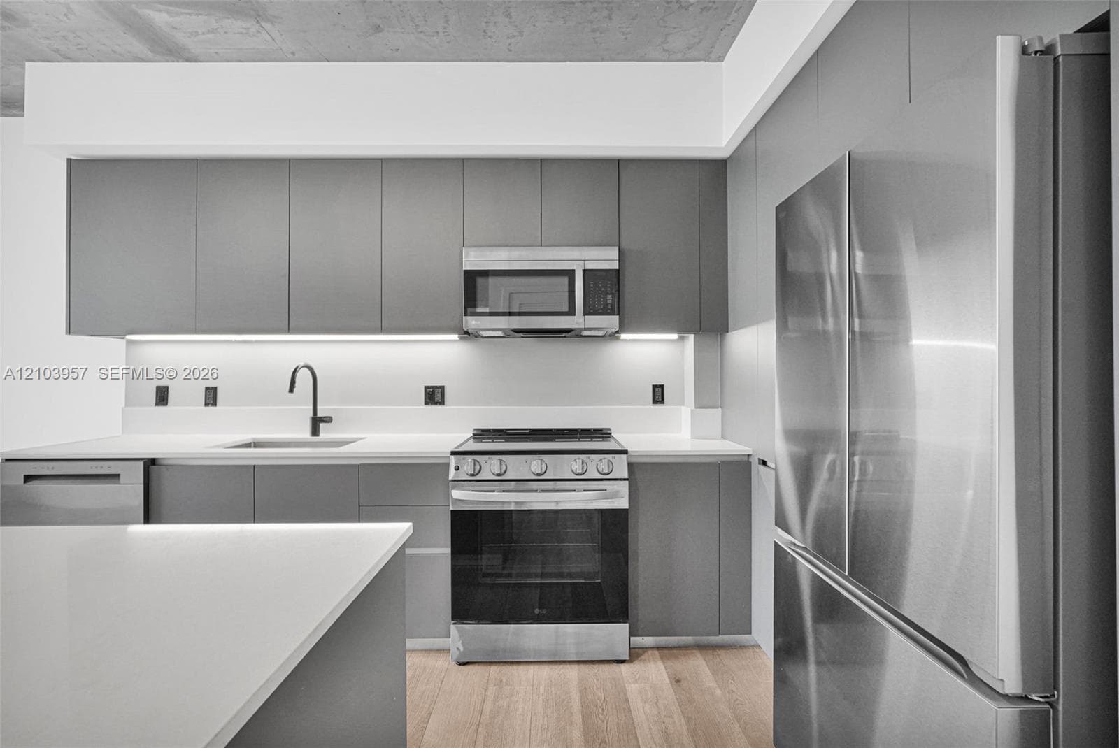 Kitchen featuring stainless steel appliances, light wood-finish flooring, white countertops, gray cabinetry, and under-cabinet lighting