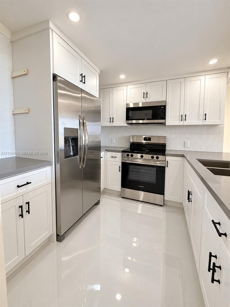 Kitchen featuring white shaker-style cabinetry, quartz countertops, stainless steel appliances, vertical tile backsplash, and polished tile flooring