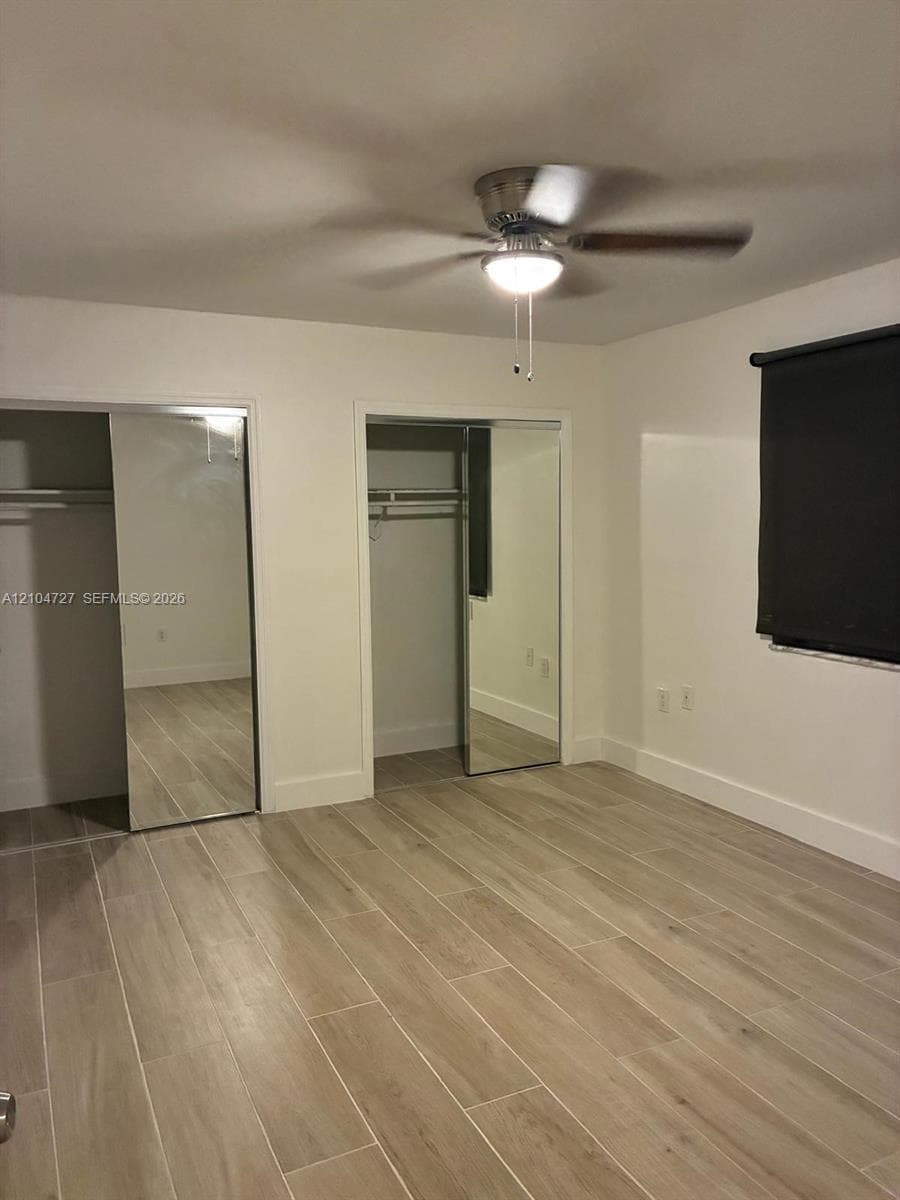 Wood-finish flooring, dual closets with mirrored sliding doors, and a ceiling-mounted light fixture with fan