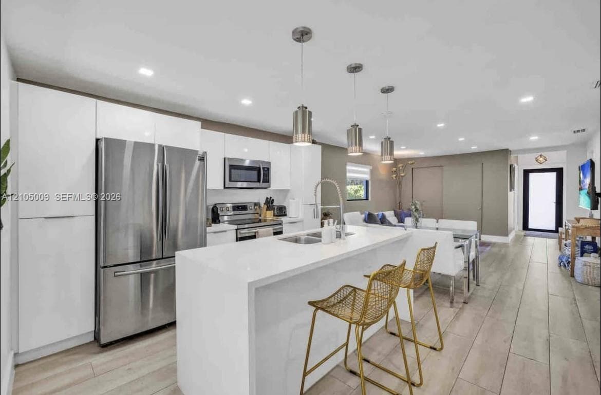 Modern kitchen featuring white cabinetry, stainless steel appliances, a center island with sink, and pendant lighting