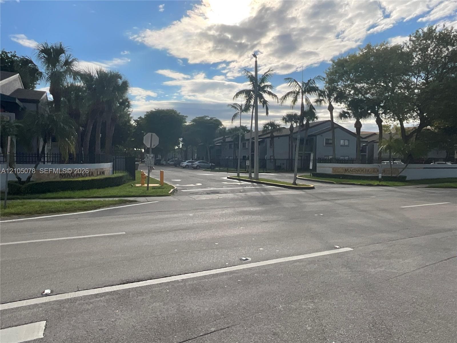 Community entrance featuring decorative stone-finish signage, mature palm trees, and manicured landscaping