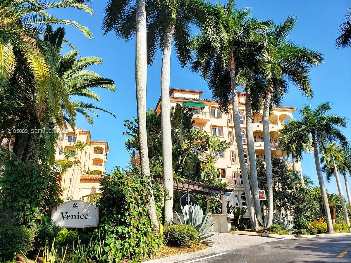 Multi-story Mediterranean-style architecture featuring stucco exterior, arched covered balconies, clay tile roof accents, and mature palm landscaping