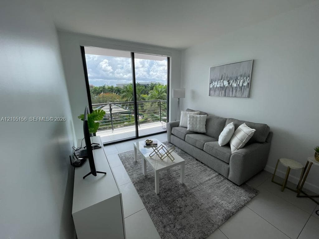 Floor-to-ceiling sliding glass doors, neutral tile flooring, and private balcony with horizontal railing