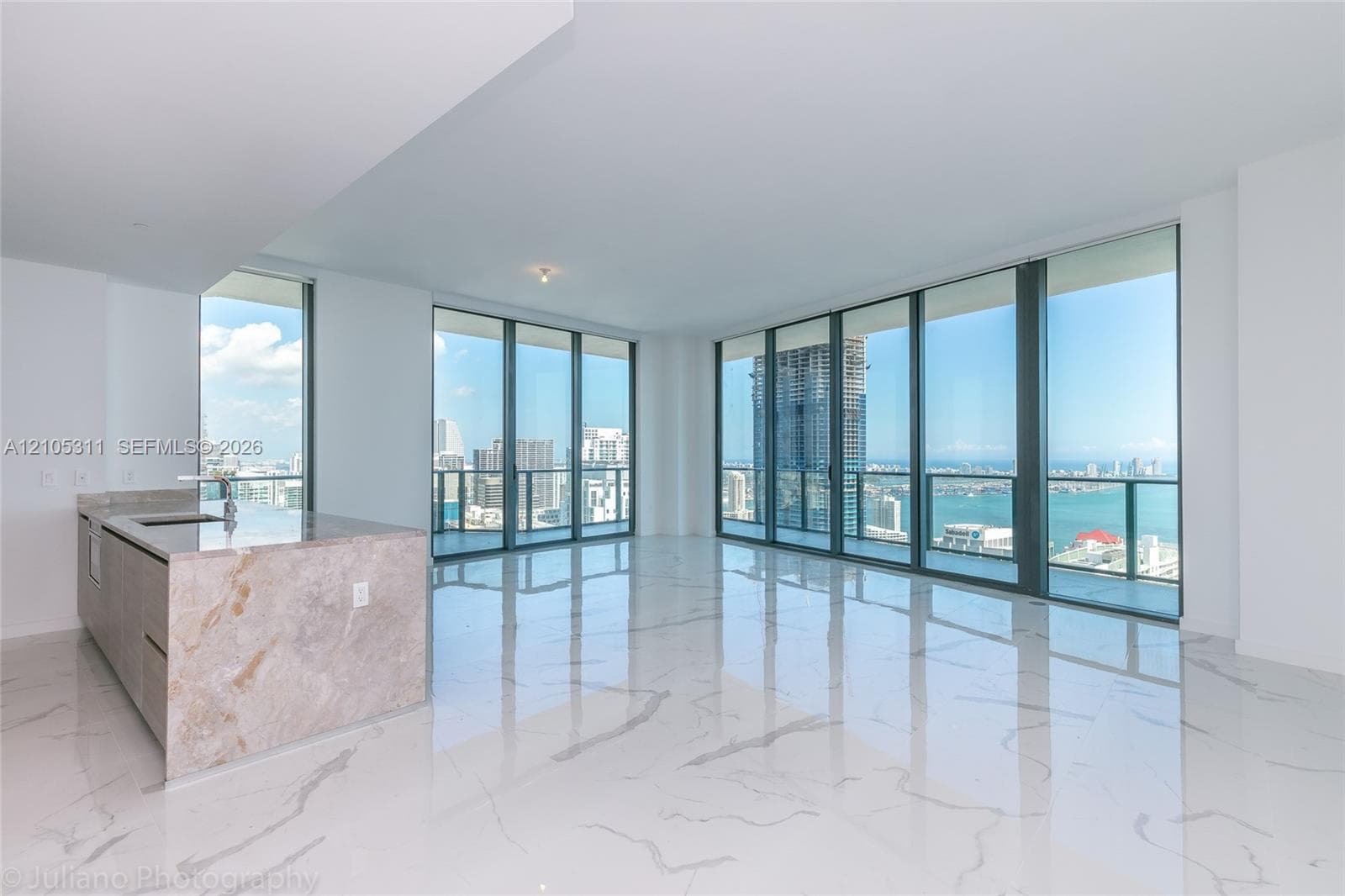 Expansive floor-to-ceiling windows, large format marble-look tile flooring, and a kitchen island with a stone countertop and integrated sink