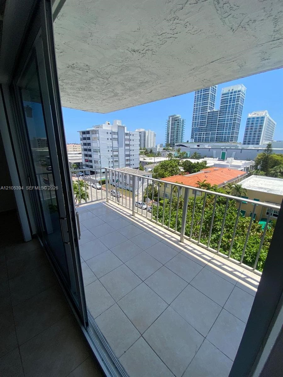 Expansive tiled balcony with metal railing, featuring sliding glass doors and a city backdrop