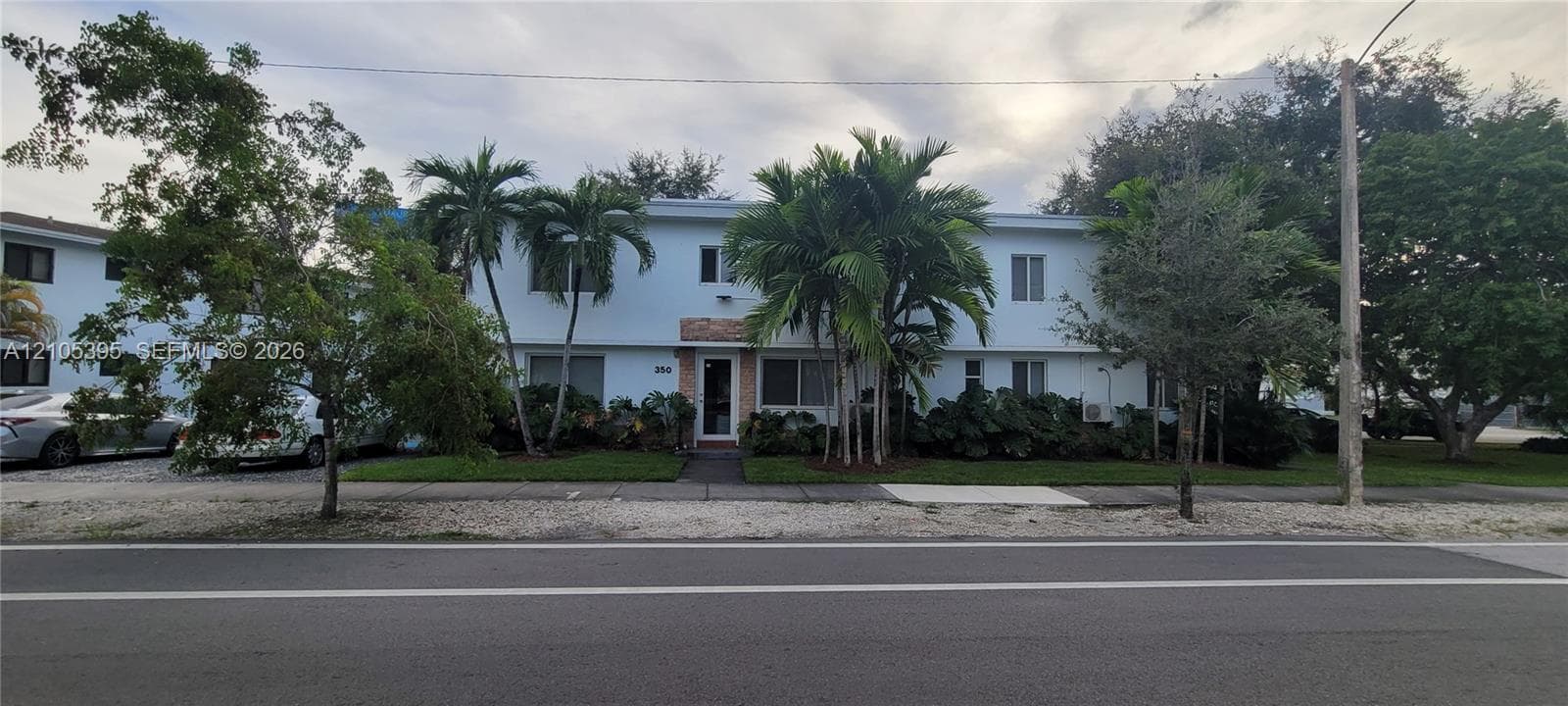 Two-story building with light blue exterior, prominent palm trees, and mature landscaping