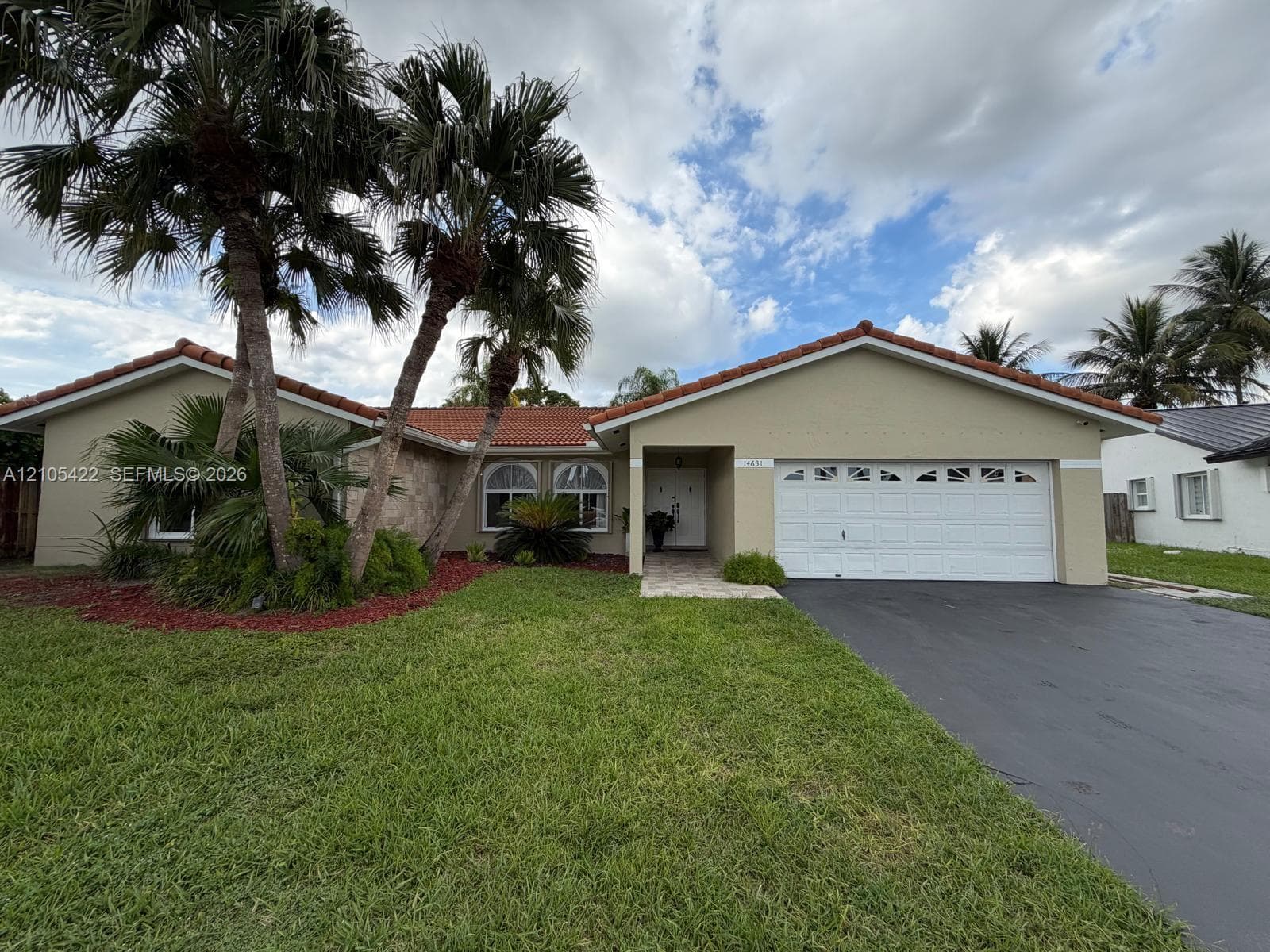 Single-story residence featuring a tile roof, arched windows, an attached two-car garage, stone facade accents, and mature palm landscaping
