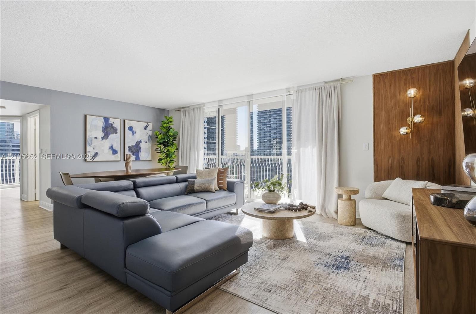 Open-concept living space featuring wood-finish flooring, floor-to-ceiling glass sliding doors, and a wood-paneled accent wall with integrated multi-globe lighting
