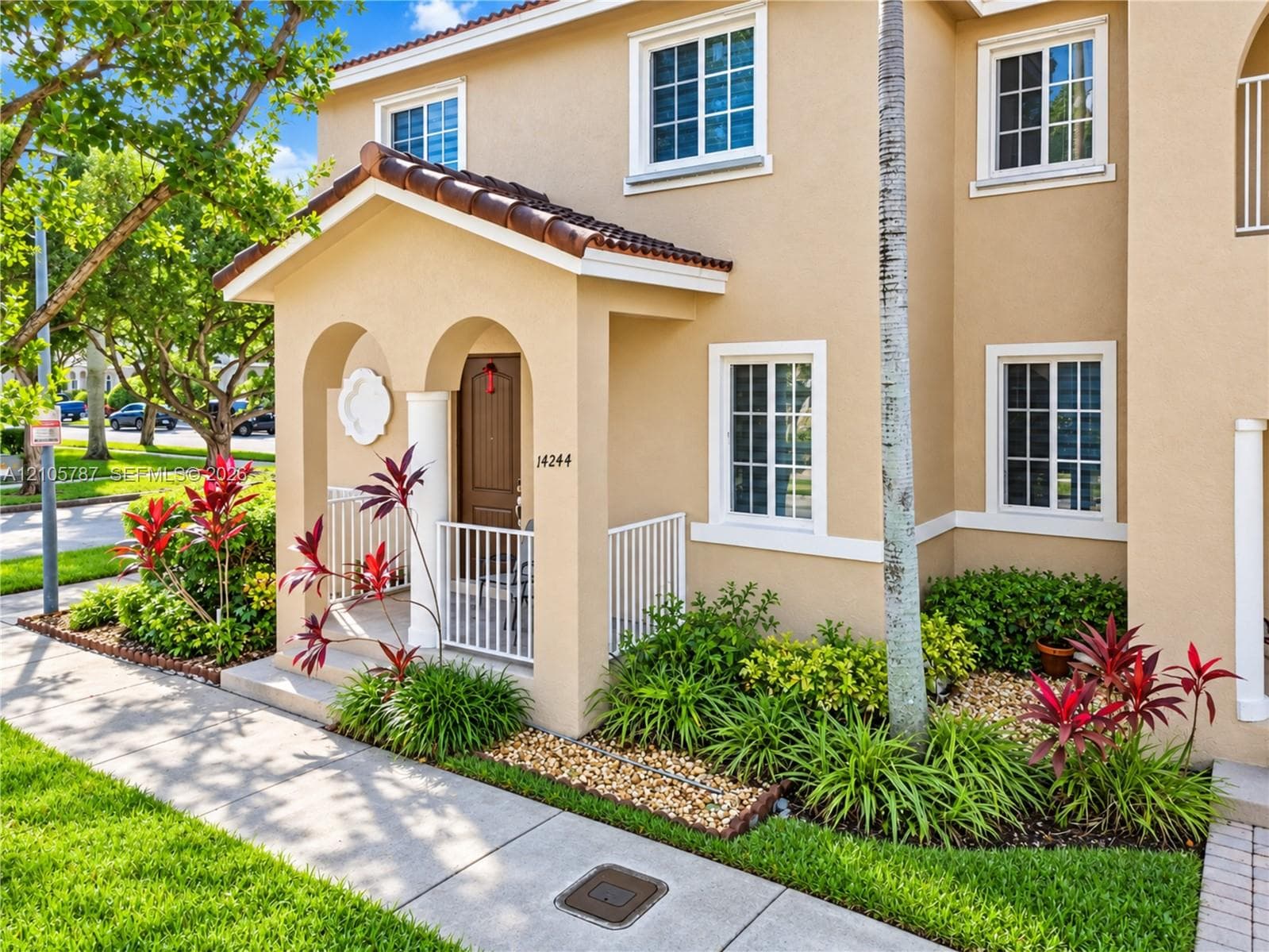 Stucco exterior featuring an arched covered entry, tiled gable roof, white metal railings, and multi-pane windows