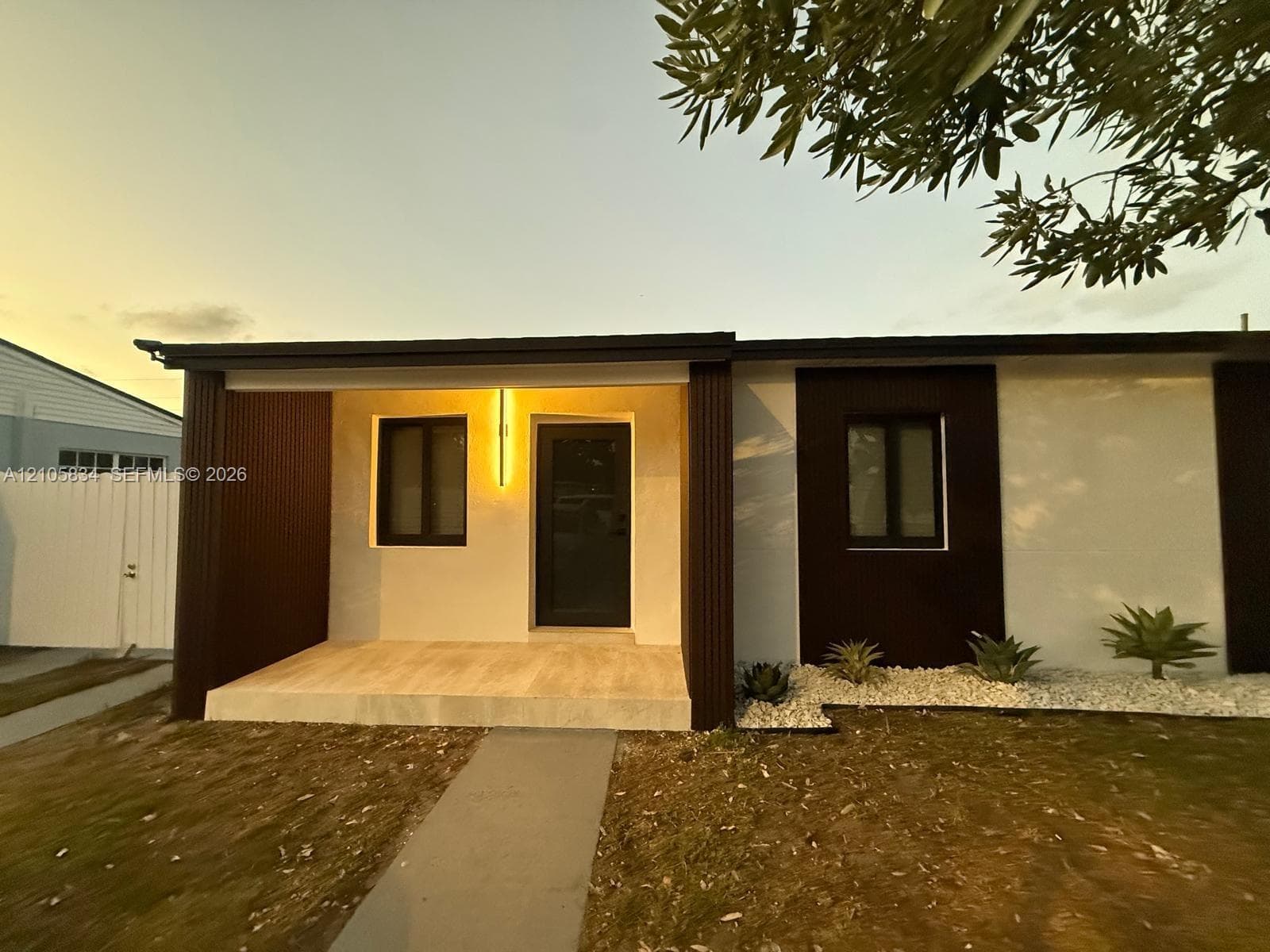 Modern facade featuring high-contrast white and dark-toned paneling, a covered front entryway, stone-tiled porch, and low-maintenance xeriscaped front garden beds
