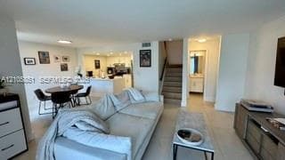 Open-concept interior featuring large-format tile flooring, recessed lighting, white cabinetry, neutral wall paint, and a built-in staircase with a wooden handrail