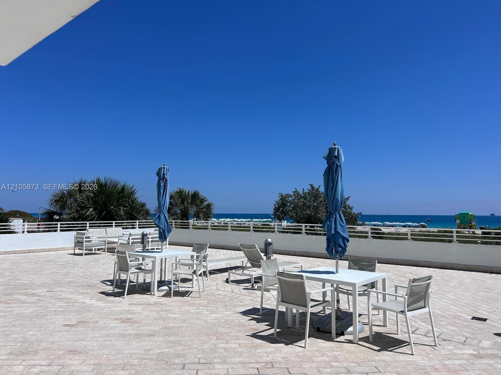 Expansive stone-paved terrace featuring a white metal perimeter railing and coastal horizon