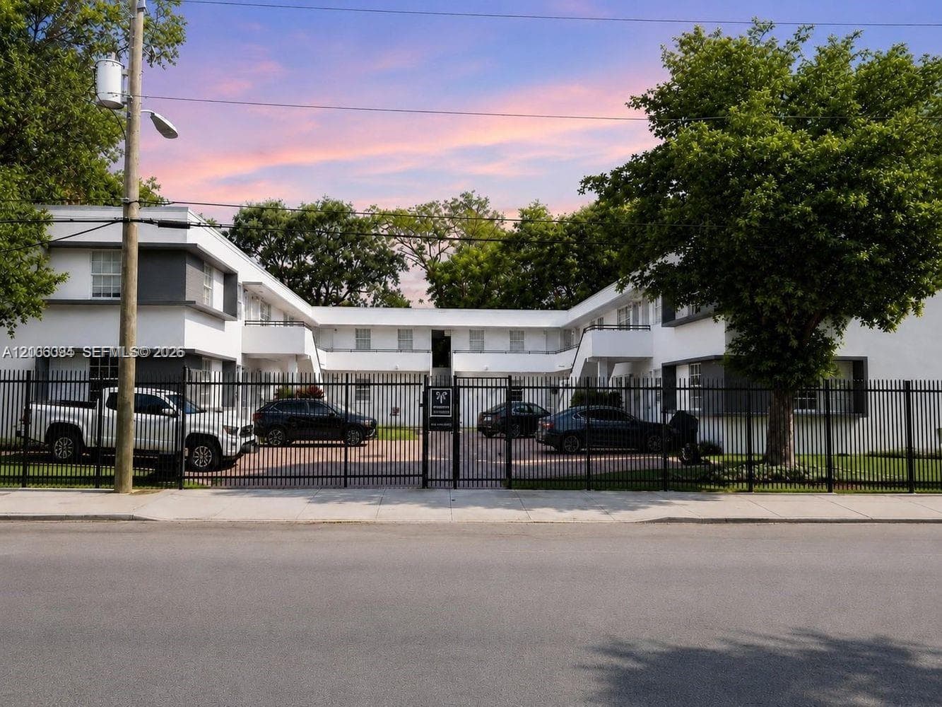 Multi-level building exterior featuring white smooth-finish siding, dark gray accents, private balconies, and a secure perimeter fence