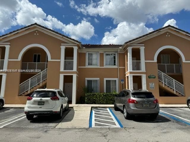 Two-story stucco exterior featuring arched entryways, covered balconies with metal railings, and dual exterior staircases