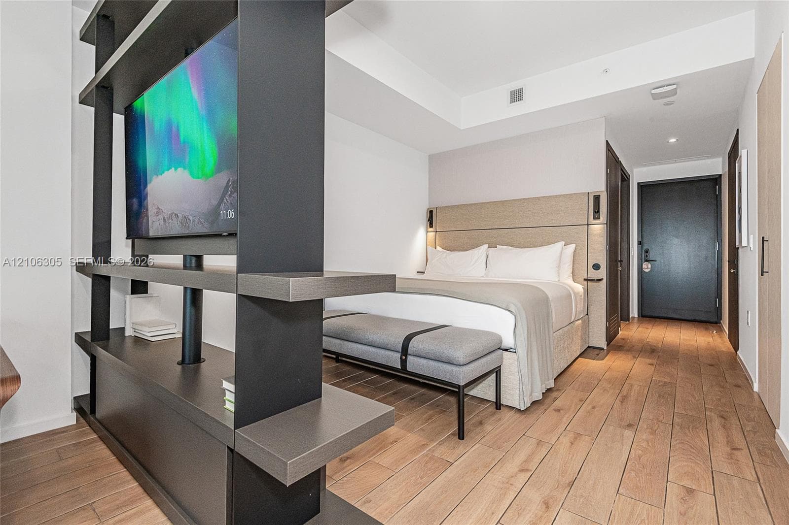 Wood-finish flooring, floor-to-ceiling built-in matte black shelving partition, and recessed ceiling lighting