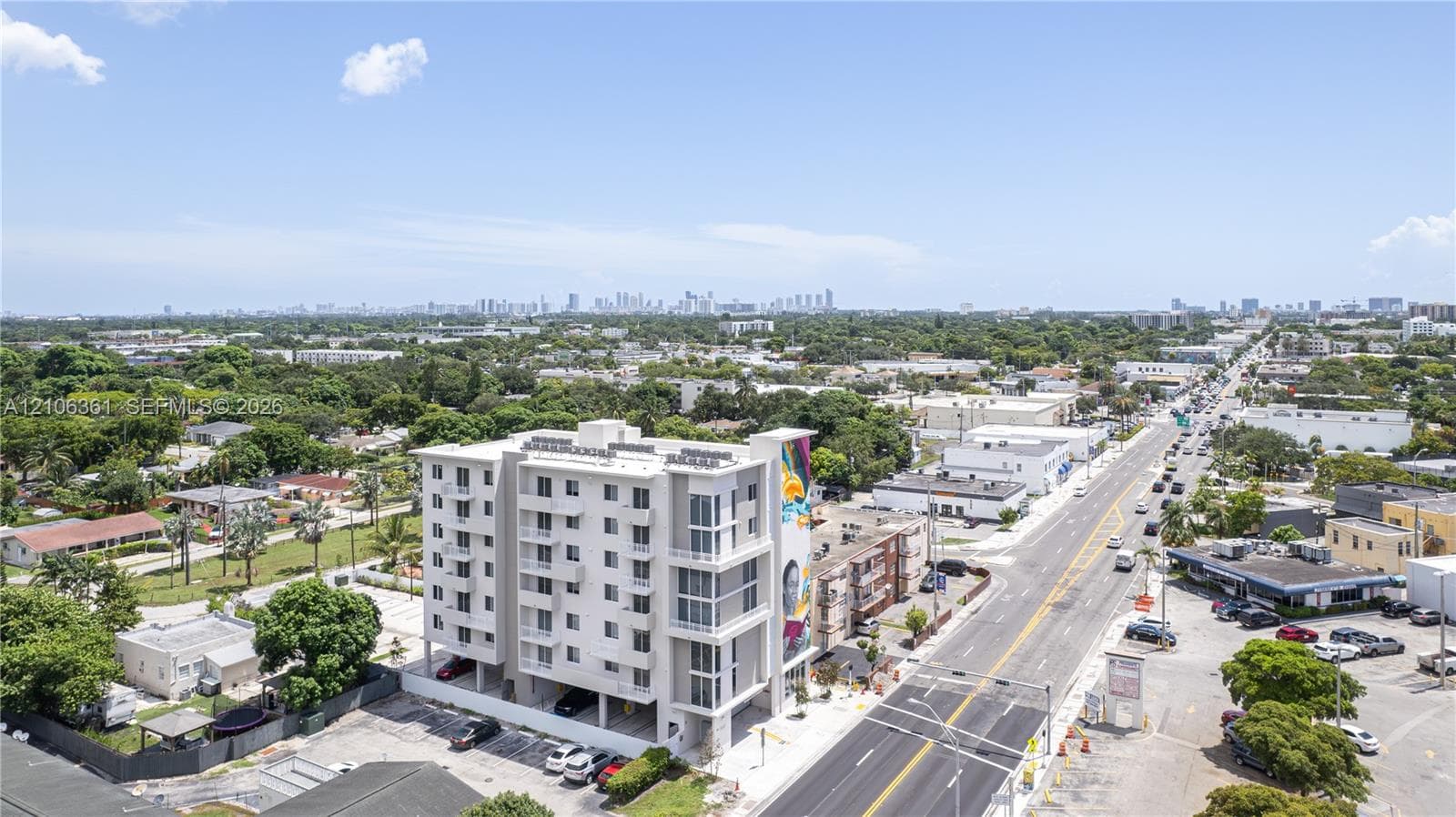 Mid-rise residential building featuring multi-level balconies, ground-level parking, and a prominent exterior mural