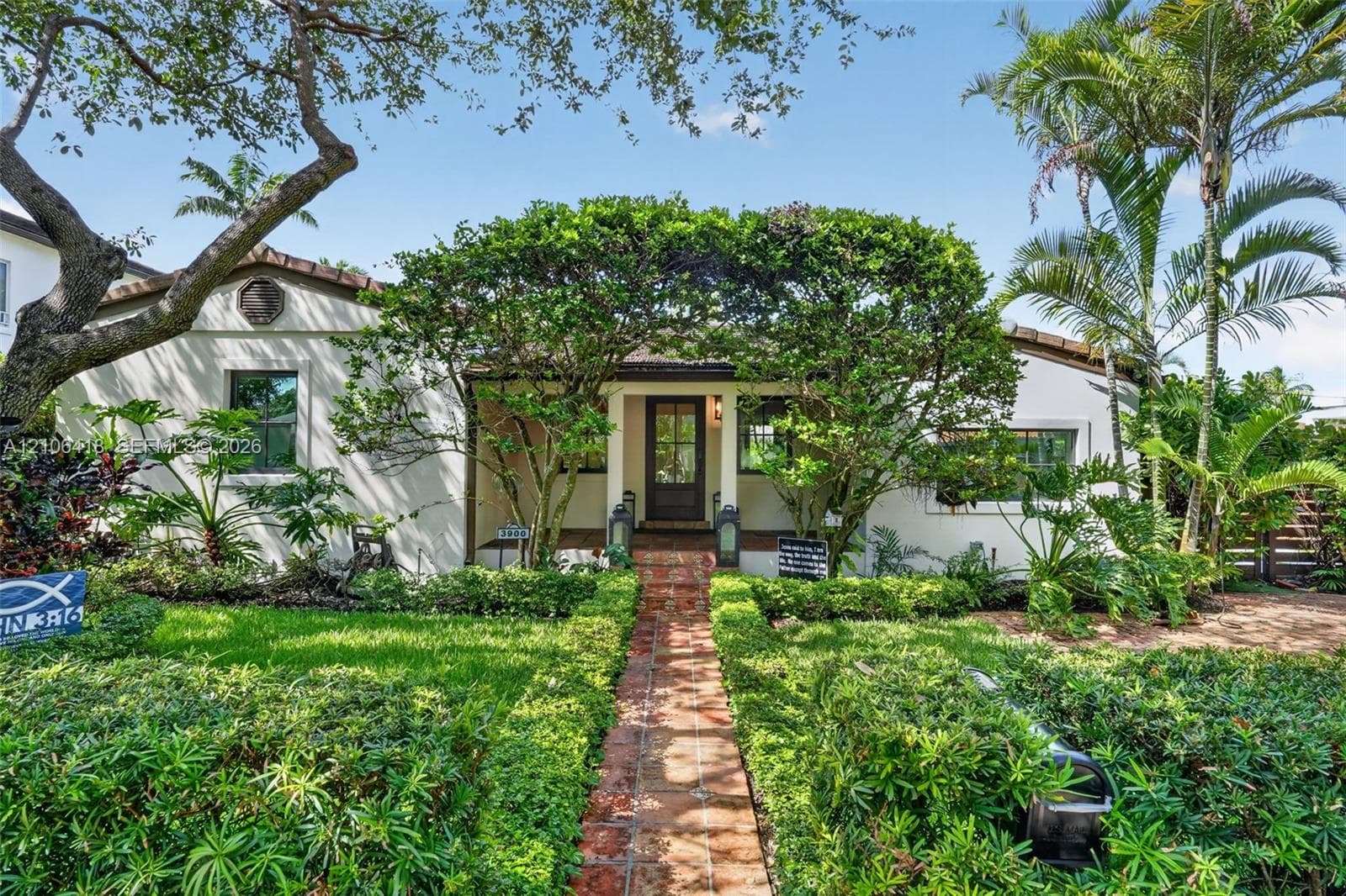 Stucco exterior residence featuring a clay tile roof, brick walkway, and landscaped garden beds