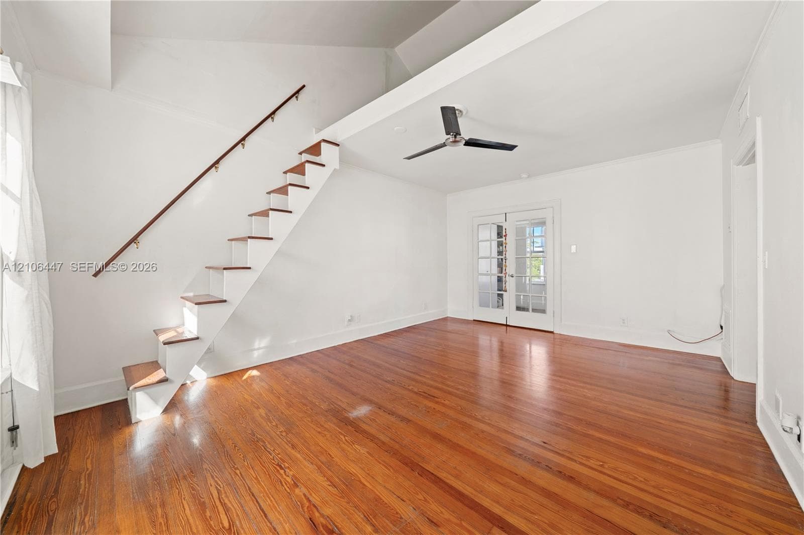 Vaulted ceiling, wood-finish flooring, staircase with wood treads and a metal handrail, ceiling fan, and French doors