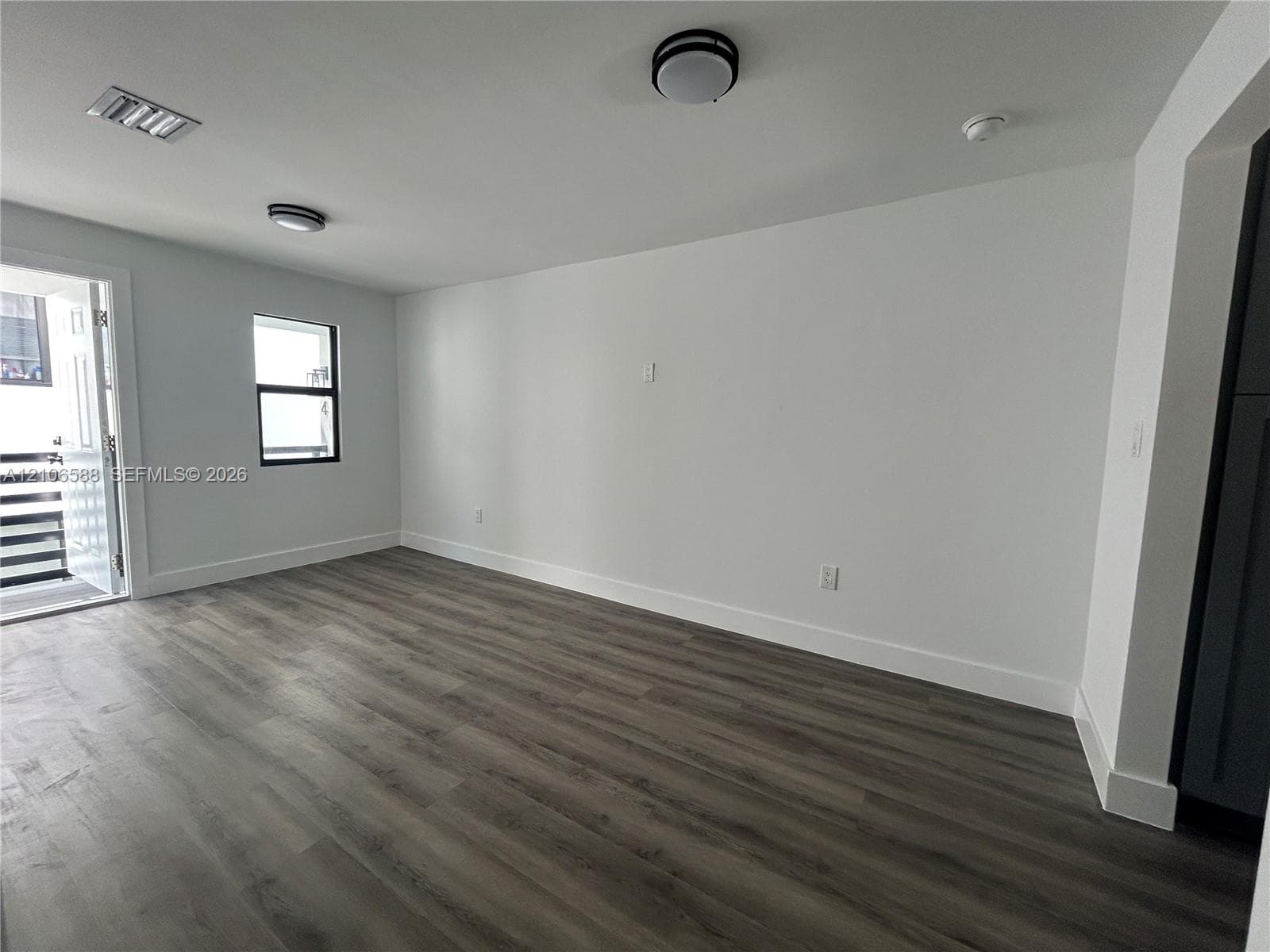 Interior space featuring wood-finish flooring, white walls, dual flush-mount ceiling light fixtures, and a single-pane window