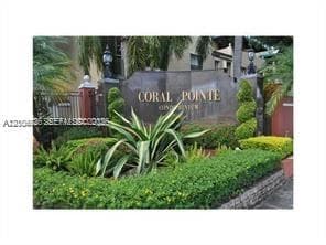 Stone monument signage featuring metallic lettering, complemented by manicured shrubbery, decorative topiary, and palm plantings