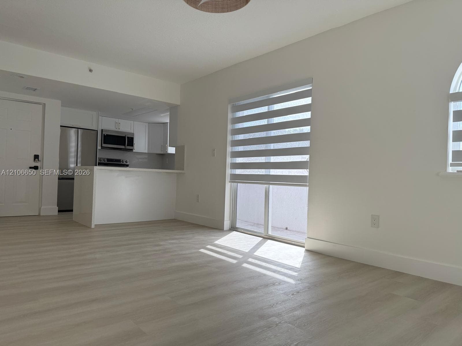 Open-concept kitchen featuring stainless steel appliances, white cabinetry, and a peninsula, complemented by wood-finish flooring and dual-tone window shades
