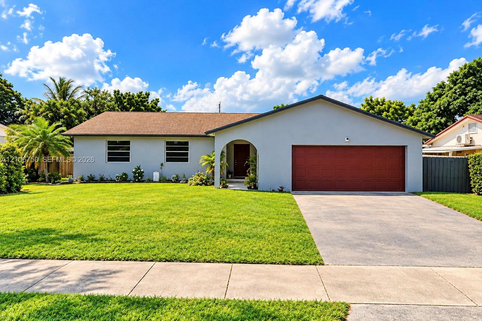 Single-story residence featuring a covered arched entryway, attached two-car garage, concrete driveway, and a front lawn with mature landscaping