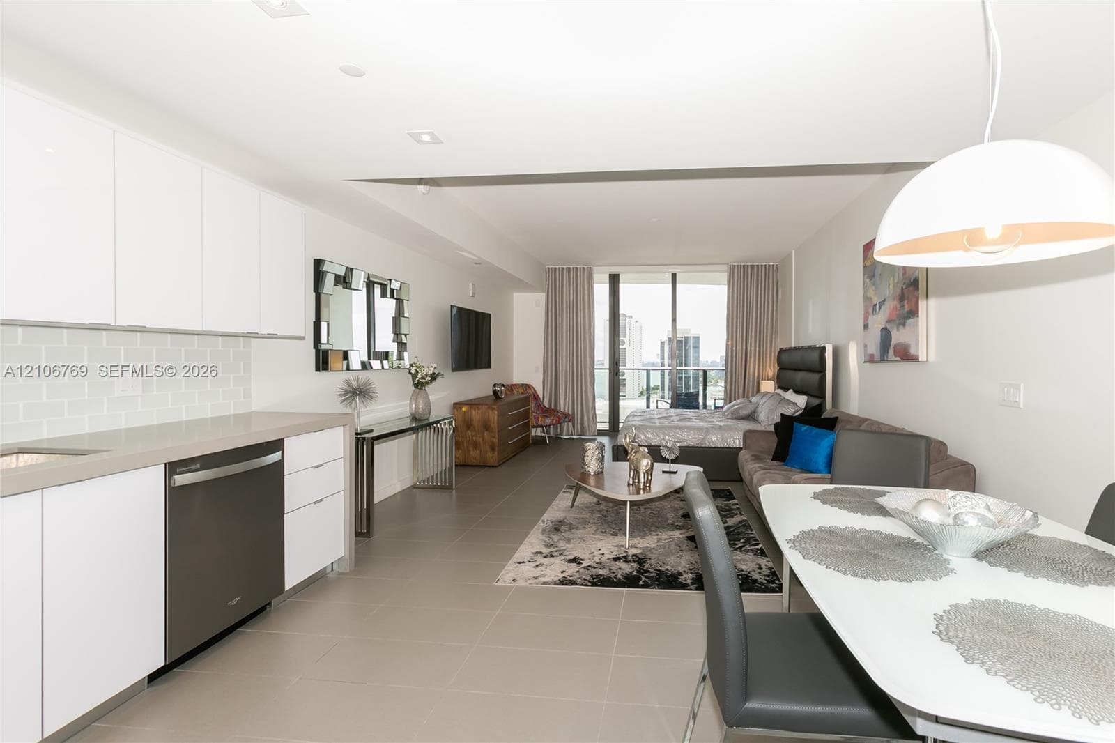 Contemporary kitchen featuring white flat-panel cabinetry, a light-toned tile backsplash, and a metallic-finish dishwasher, complemented by large-format floor tiling and floor-to-ceiling glass patio doors