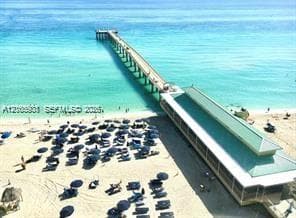 Aerial perspective of a coastal pier with a pitched metal roof, sandy beachfront, and direct ocean access