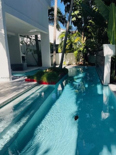 Lap-style swimming pool featuring submerged entry steps, a raised central landscape island, and an integrated water feature wall