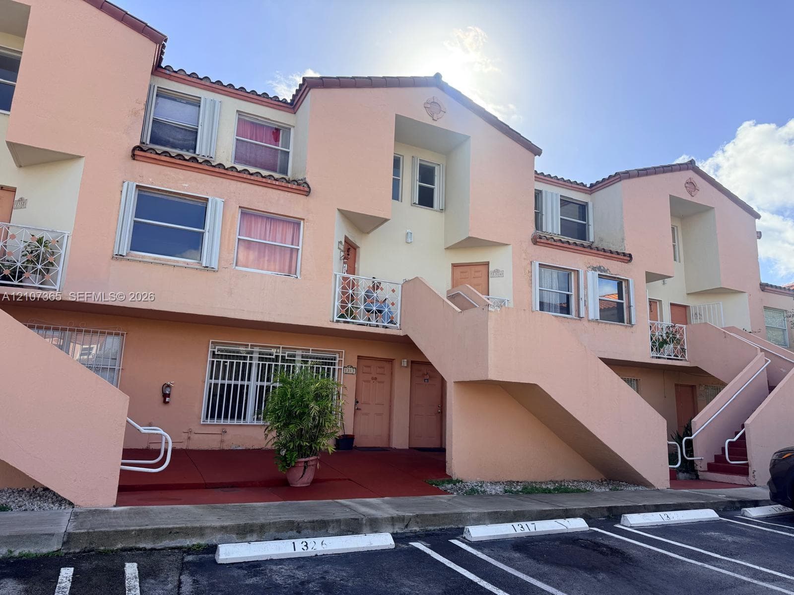 Multi-level exterior featuring stucco siding, tiled roof accents, metal window security bars, and concrete staircases with integrated handrails