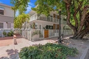 Two-story residential exterior featuring white stucco siding, full-length upper and lower level balconies, metal fencing, and mature landscaping