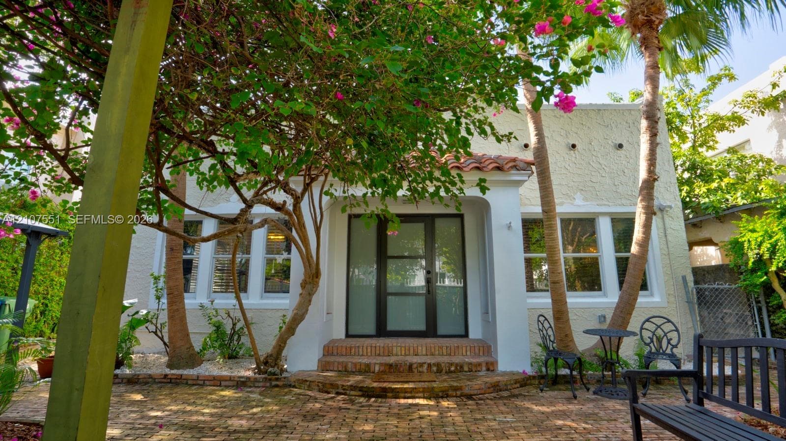 Stucco exterior featuring a brick-paved patio, tile roof accents, and a contemporary multi-panel glass entry door