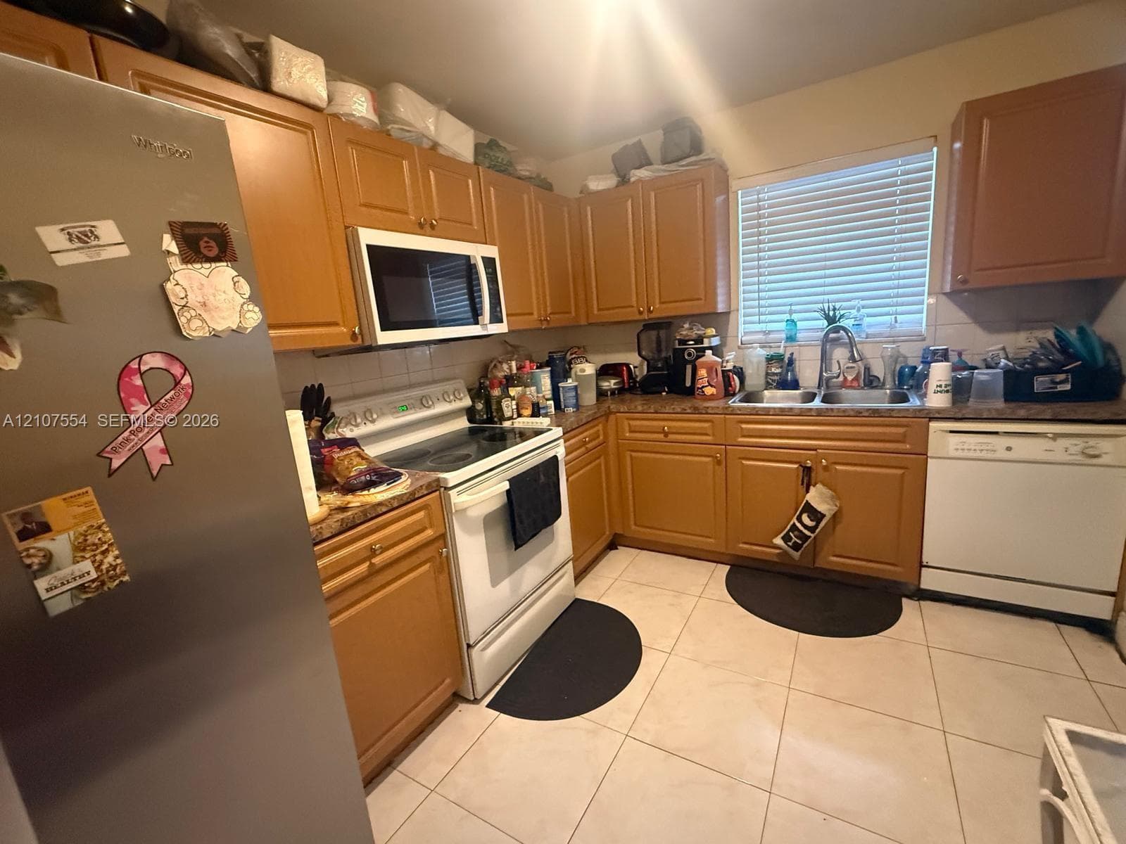 Kitchen featuring wood cabinetry, tile flooring, stainless steel refrigerator, white appliance package, and double basin sink